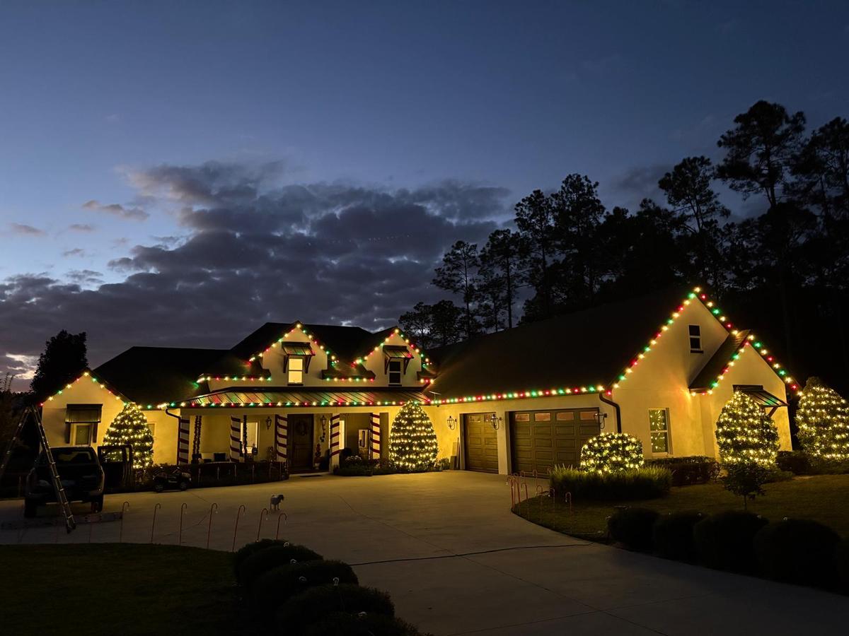 Craftsman home with warm white roofline and wrapped bushes at dusk