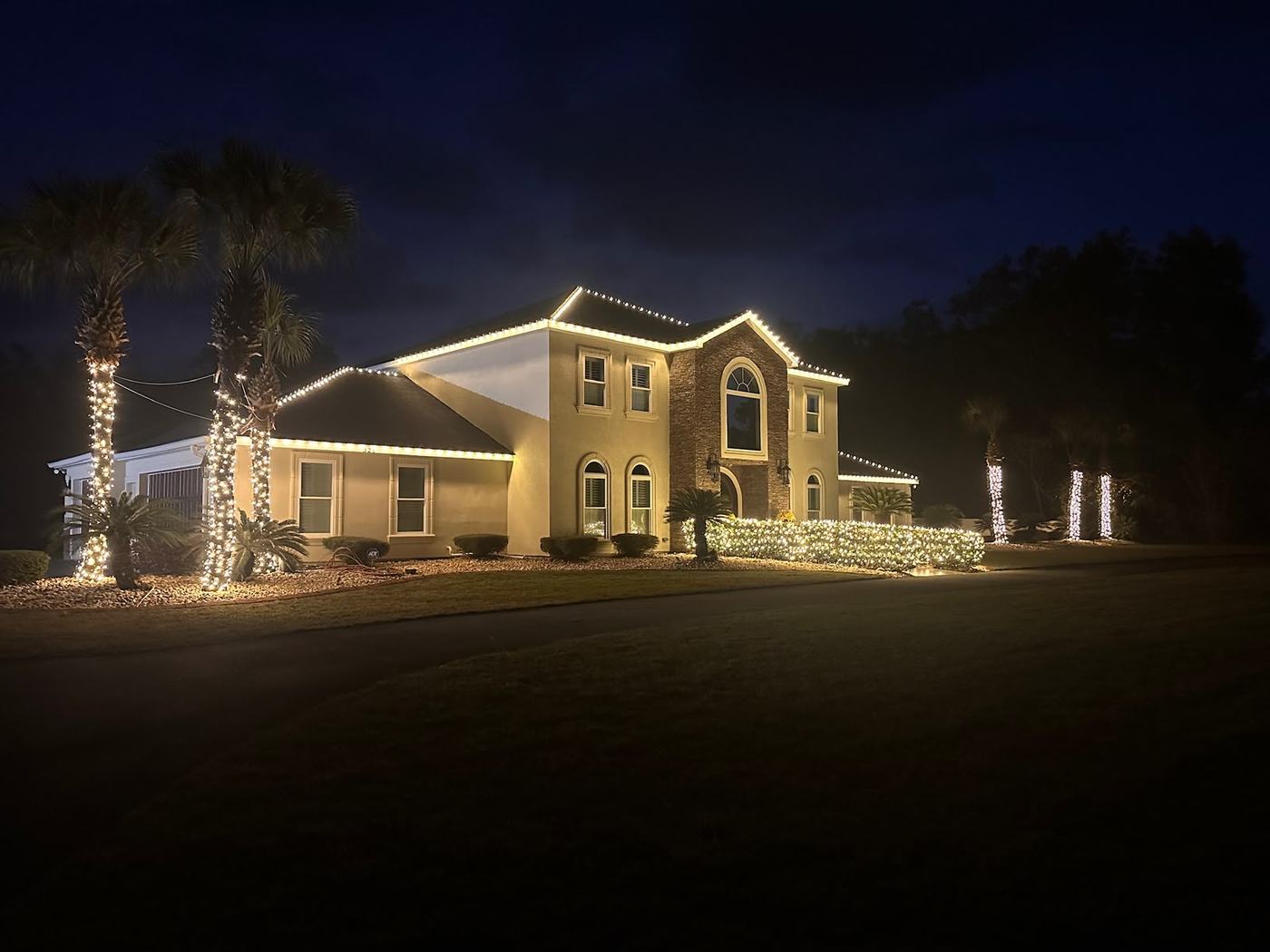 Warm white roofline lighting and wrapped trees on a Houston home